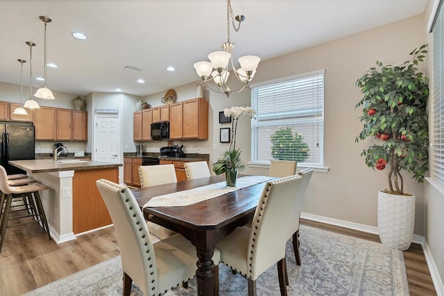 dining room with light wood-type flooring, sink, and a notable chandelier