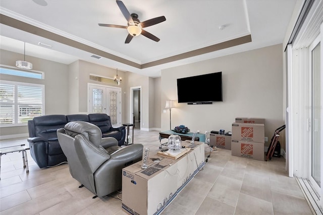 living room with ceiling fan with notable chandelier, crown molding, and a tray ceiling