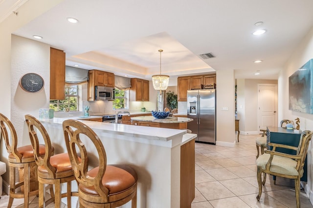 kitchen featuring pendant lighting, light tile patterned flooring, kitchen peninsula, a raised ceiling, and appliances with stainless steel finishes