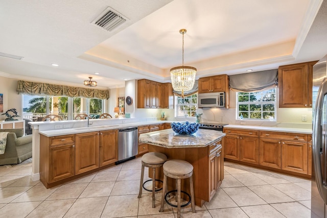 kitchen featuring decorative light fixtures, appliances with stainless steel finishes, a raised ceiling, and a kitchen island