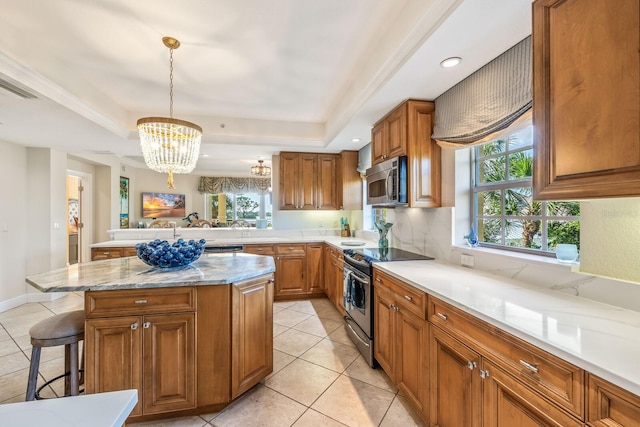 kitchen with a tray ceiling, a chandelier, stainless steel appliances, and decorative light fixtures