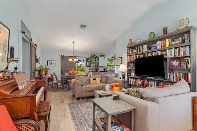 living room with a barn door, visible vents, an inviting chandelier, vaulted ceiling, and light wood-style floors