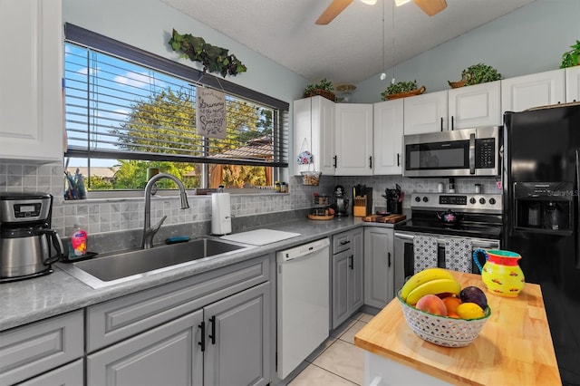 kitchen with butcher block counters, appliances with stainless steel finishes, vaulted ceiling, a sink, and light tile patterned flooring