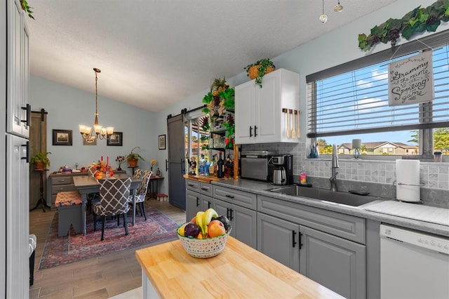 kitchen featuring butcher block counters, a barn door, vaulted ceiling, a sink, and dishwasher