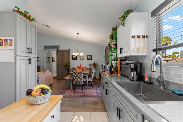 kitchen featuring sink, backsplash, white cabinetry, light wood-type flooring, and vaulted ceiling