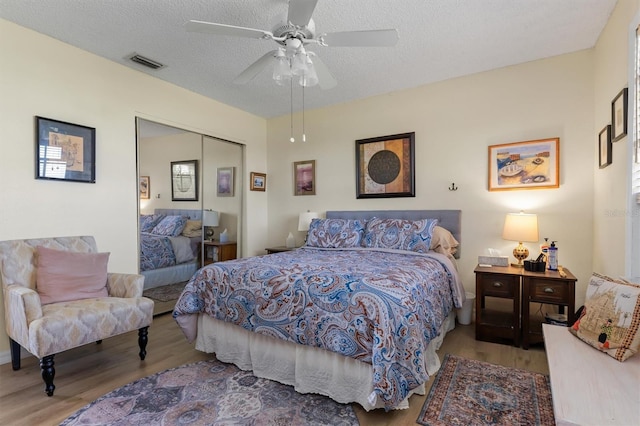 bedroom with a closet, visible vents, a textured ceiling, and wood finished floors