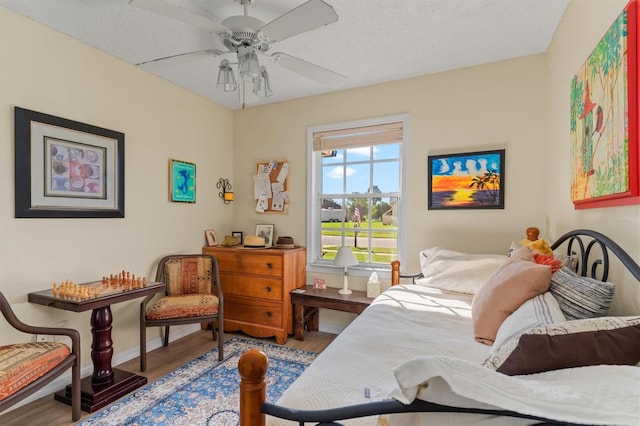 bedroom with ceiling fan, a textured ceiling, baseboards, and wood finished floors