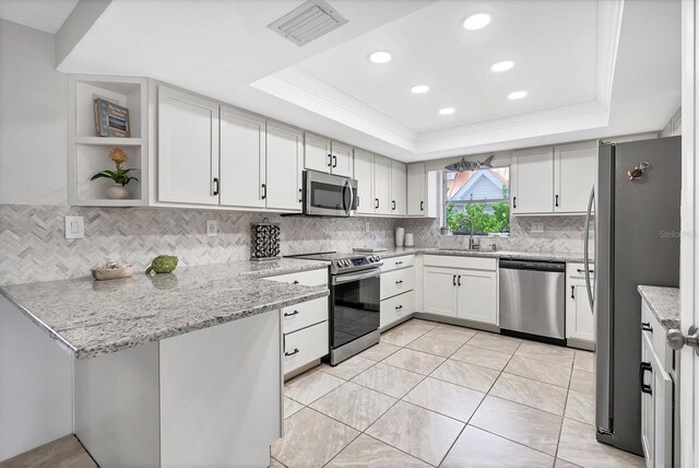 kitchen featuring sink, light stone countertops, appliances with stainless steel finishes, a tray ceiling, and white cabinetry