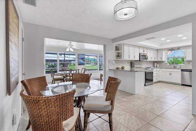 tiled dining room featuring a tray ceiling, ceiling fan, and sink