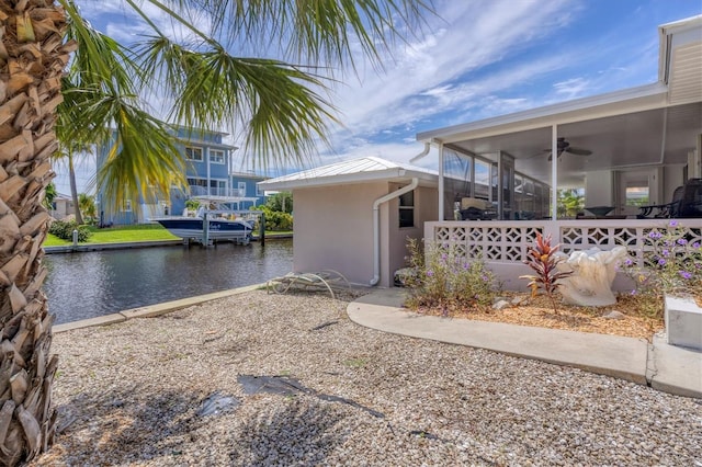 view of yard with a sunroom, ceiling fan, a dock, and a water view