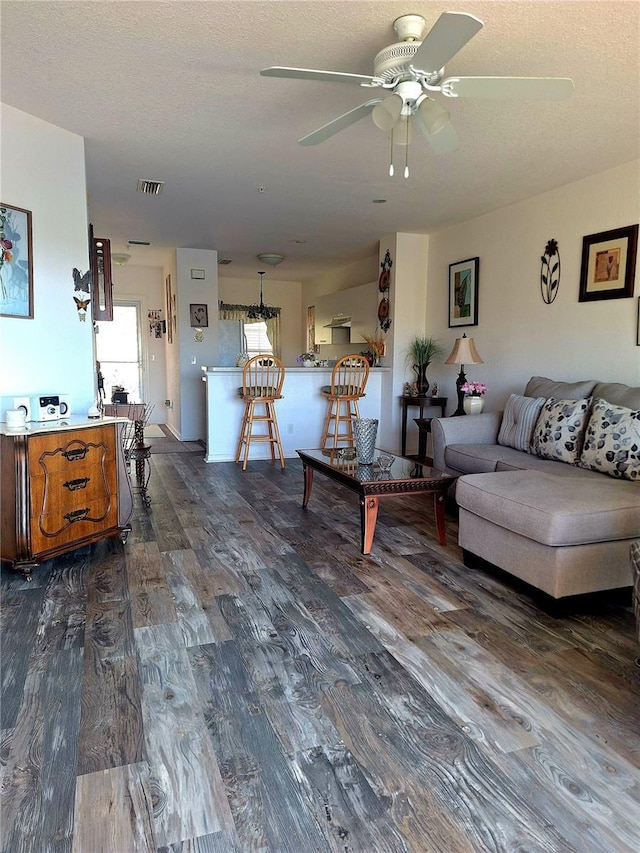 living room with a textured ceiling, ceiling fan, and dark wood-type flooring