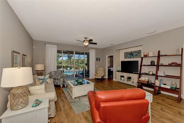 living room featuring light hardwood / wood-style flooring, ceiling fan, and a textured ceiling