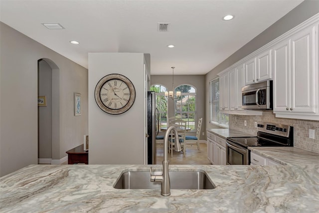 kitchen with sink, white cabinetry, appliances with stainless steel finishes, a notable chandelier, and light stone countertops