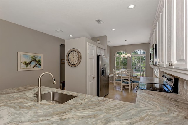 kitchen featuring appliances with stainless steel finishes, hanging light fixtures, white cabinets, sink, and a notable chandelier