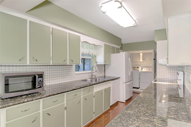 kitchen with wood-type flooring, sink, separate washer and dryer, dark stone counters, and decorative backsplash