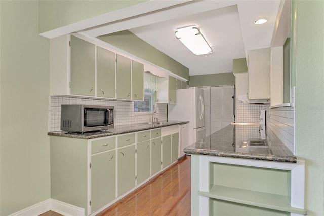 kitchen with tasteful backsplash, green cabinets, light hardwood / wood-style floors, stainless steel appliances, and dark stone counters