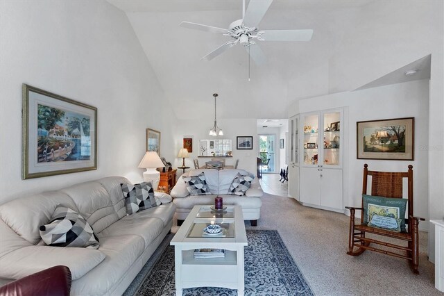 carpeted living room featuring ceiling fan with notable chandelier and high vaulted ceiling