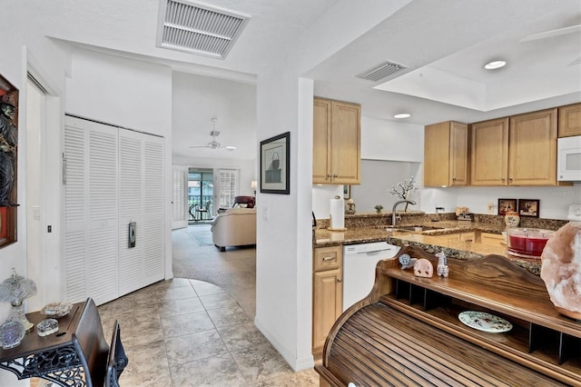 kitchen with dark stone countertops, white appliances, light brown cabinetry, ceiling fan, and sink