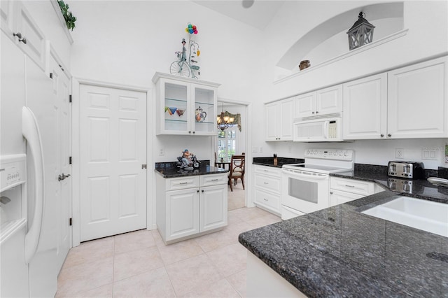 kitchen featuring dark stone counters, light tile patterned flooring, white cabinetry, high vaulted ceiling, and white appliances