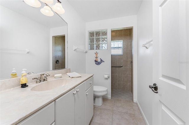 bathroom with a tile shower, tile patterned flooring, vanity, and toilet