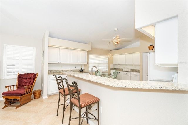 kitchen with a kitchen breakfast bar, vaulted ceiling, light stone counters, kitchen peninsula, and ceiling fan