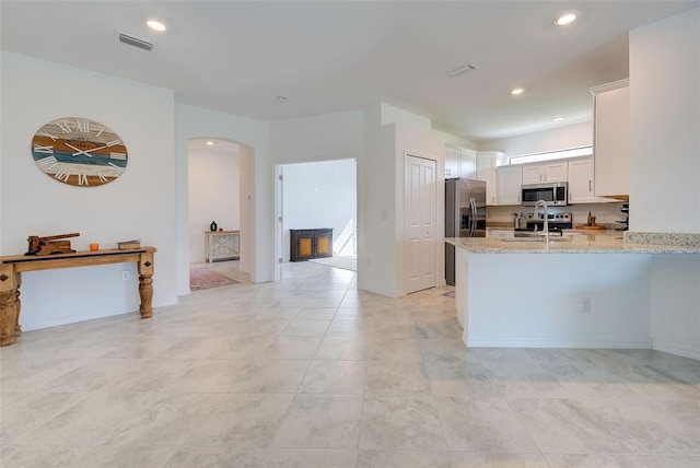 kitchen featuring light stone counters, sink, white cabinets, kitchen peninsula, and appliances with stainless steel finishes