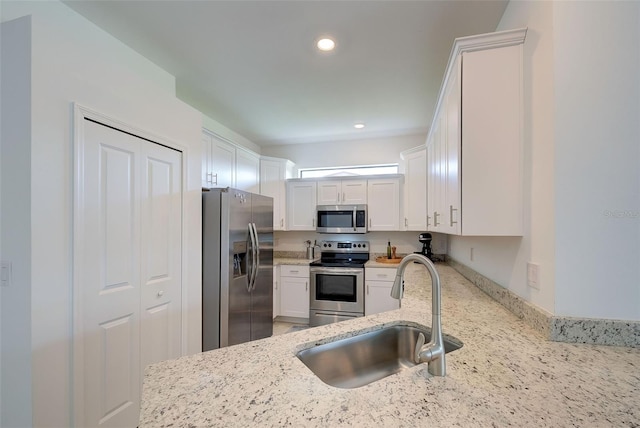 kitchen with appliances with stainless steel finishes, sink, light stone counters, and white cabinets