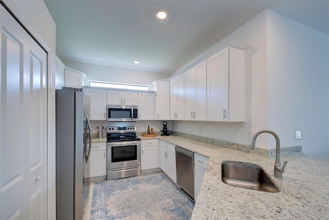 kitchen featuring stainless steel appliances, white cabinetry, light stone counters, and sink