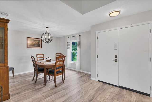 dining area with a textured ceiling, a chandelier, and light hardwood / wood-style floors