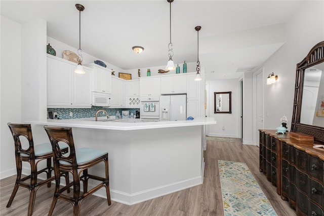 11100 Hacienda Del Mar Blvd Unit 202, Placida, FL 33946 - kitchen with a peninsula, light wood finished floors, white appliances, tasteful backsplash, and white cabinetry