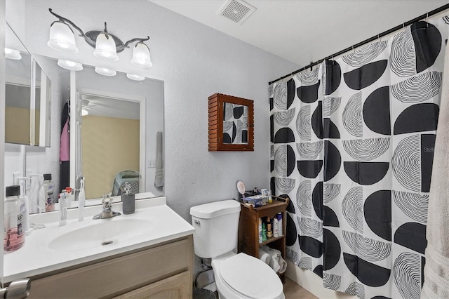 full bath with ceiling fan, a textured wall, toilet, vanity, and visible vents