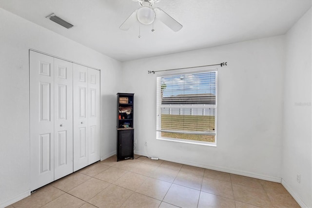 unfurnished bedroom with light tile patterned floors, visible vents, baseboards, ceiling fan, and a closet