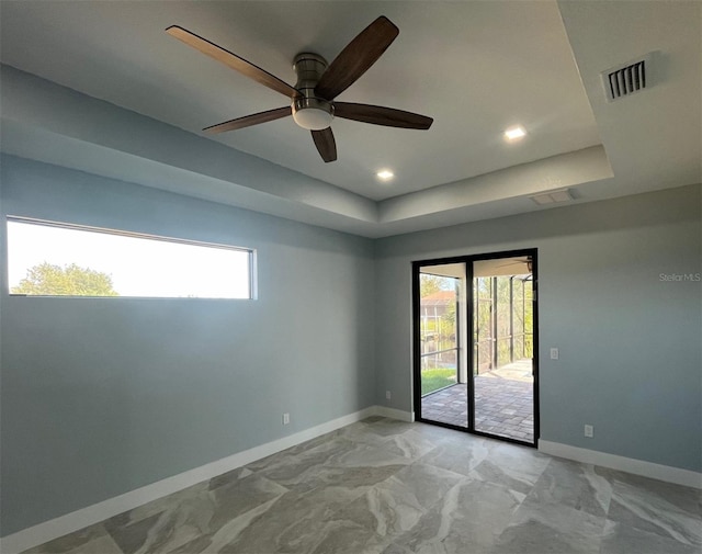 unfurnished room featuring a tray ceiling, a ceiling fan, visible vents, and a healthy amount of sunlight