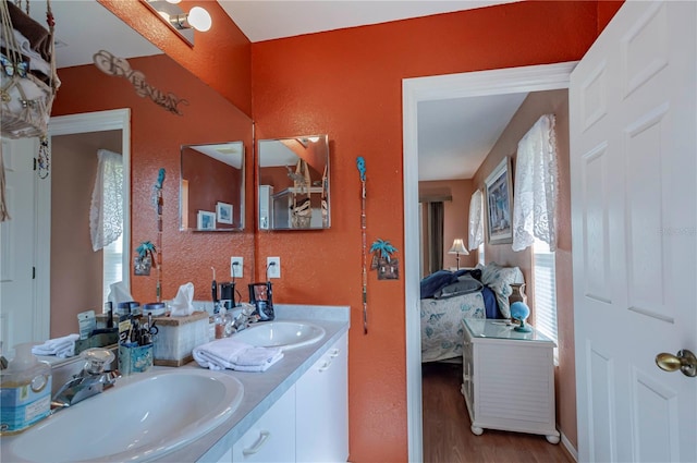 full bath with connected bathroom, double vanity, a sink, and wood finished floors