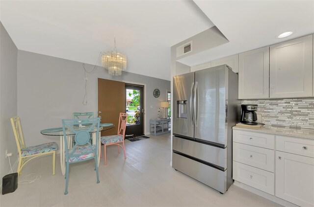 kitchen featuring white cabinets, stainless steel refrigerator with ice dispenser, an inviting chandelier, backsplash, and decorative light fixtures