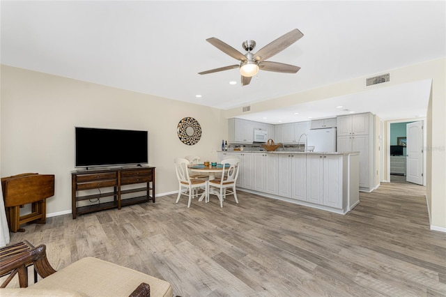 kitchen with kitchen peninsula, light wood-type flooring, white appliances, and ceiling fan