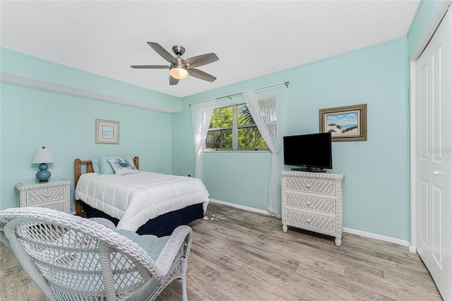 bedroom featuring a closet, light hardwood / wood-style floors, ceiling fan, and wood walls