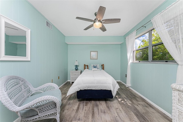 bedroom featuring ceiling fan, dark hardwood / wood-style flooring, and wooden walls