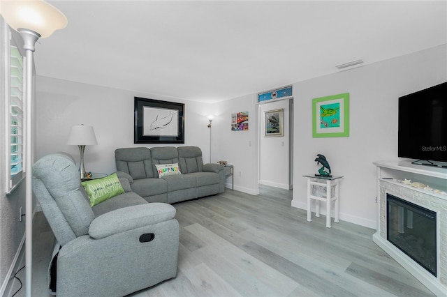 living room with visible vents, baseboards, light wood-style floors, and a glass covered fireplace