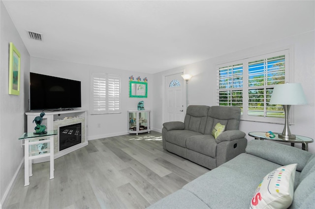 living room featuring a glass covered fireplace, visible vents, baseboards, and wood finished floors