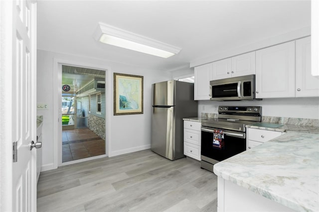 kitchen with light stone counters, light wood-type flooring, appliances with stainless steel finishes, and white cabinets