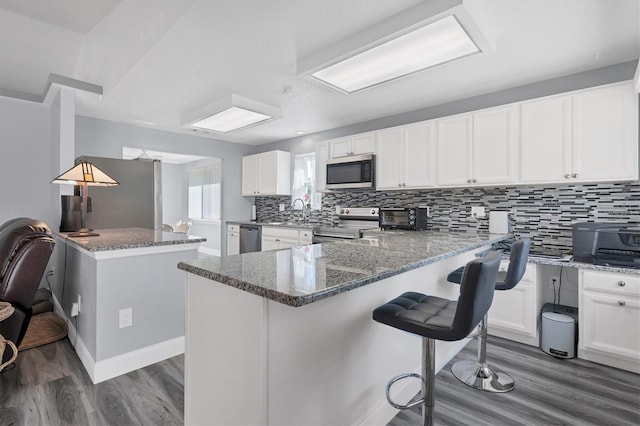 kitchen featuring a breakfast bar, dark hardwood / wood-style floors, white cabinets, kitchen peninsula, and appliances with stainless steel finishes