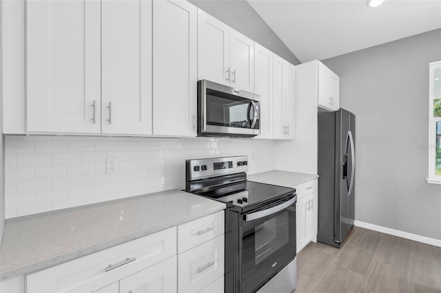 kitchen featuring white cabinets, vaulted ceiling, decorative backsplash, appliances with stainless steel finishes, and light stone countertops