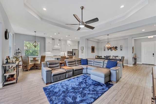 living room featuring ceiling fan with notable chandelier, ornamental molding, a raised ceiling, and light hardwood / wood-style floors