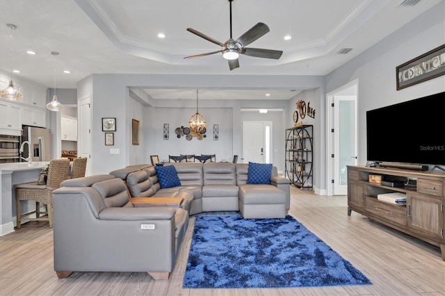 living room with ceiling fan with notable chandelier, ornamental molding, a raised ceiling, and light hardwood / wood-style floors