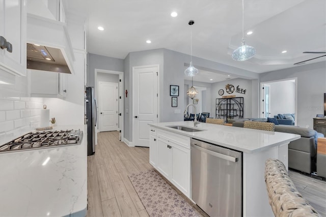 kitchen with appliances with stainless steel finishes, hanging light fixtures, white cabinetry, an island with sink, and sink