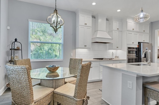 kitchen with pendant lighting, an island with sink, light hardwood / wood-style flooring, appliances with stainless steel finishes, and custom range hood