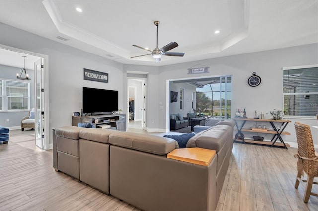 living room featuring ceiling fan with notable chandelier, a raised ceiling, crown molding, and light hardwood / wood-style flooring