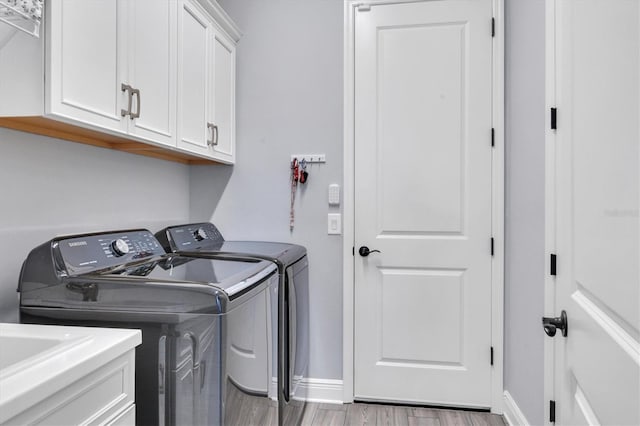 washroom featuring washer and clothes dryer, cabinets, and light wood-type flooring