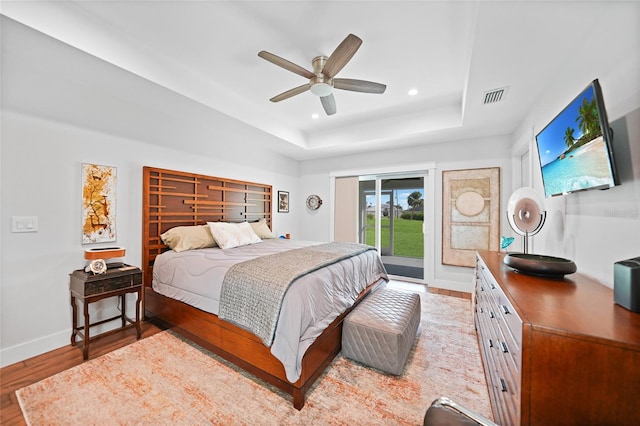 bedroom with light wood-type flooring, a tray ceiling, ceiling fan, and access to exterior